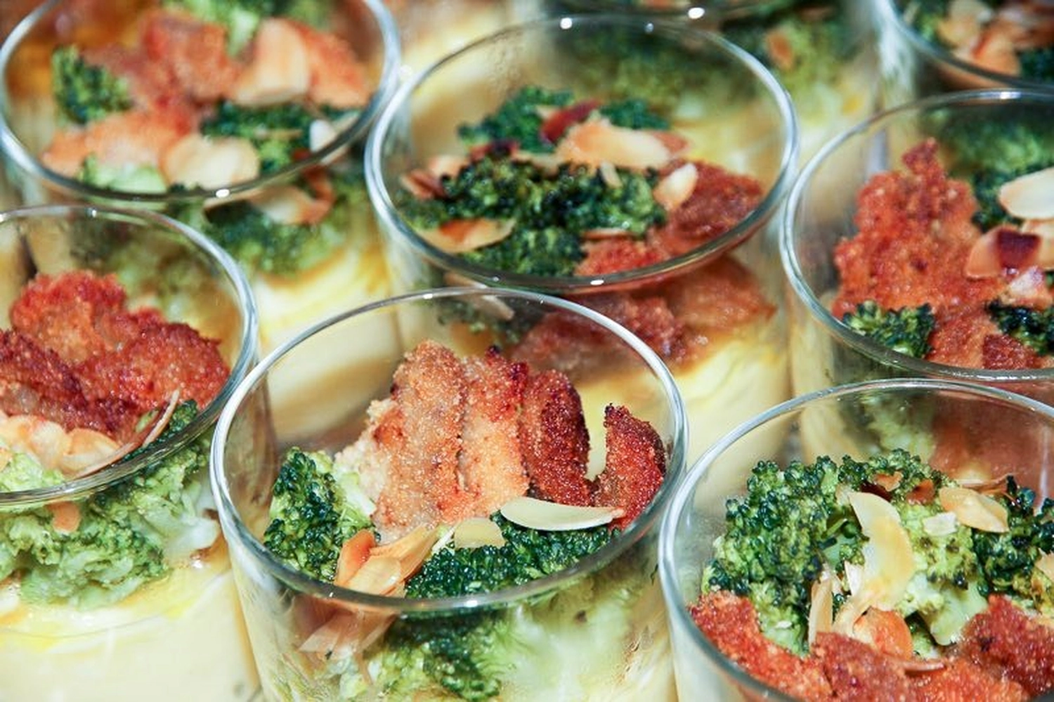 Thörnich – EventCatering – Einzelne Portionen Brokkoli-Gratin, wahrscheinlich als Vorspeise oder Beilage serviert. Gratin ist ein Gericht, das typischerweise mit einer gebräunten Kruste aus Semmelbröseln, Käse oder Butter belegt ist.